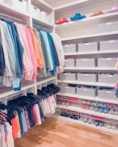 Closet with pastel-colored clothes hanging and organized shoe storage on shelves.