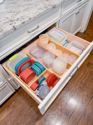 Open kitchen drawer filled with various plastic food containers and lids.
