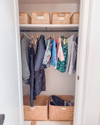 Clothes hanging in a closet with storage baskets on a shelf above and baskets on the floor below.