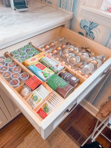 Drawer open with coffee pods, tea bags, and silver foil-wrapped chocolates, organized in compartments.