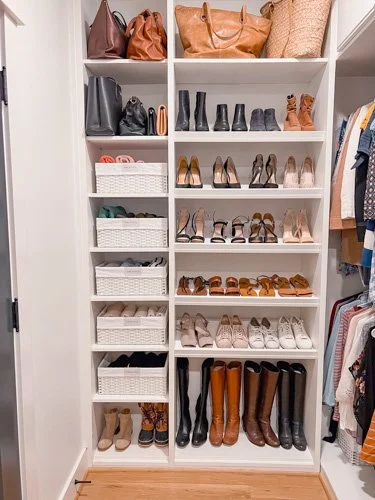 White closet with organized shoe shelves filled with various heels, boots, and sandals, and handbags on top.