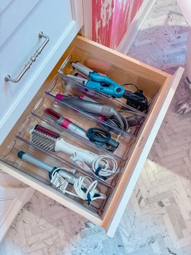 Drawer containing various hair styling tools including curling irons, a straightener, a brush, and a hairdryer.