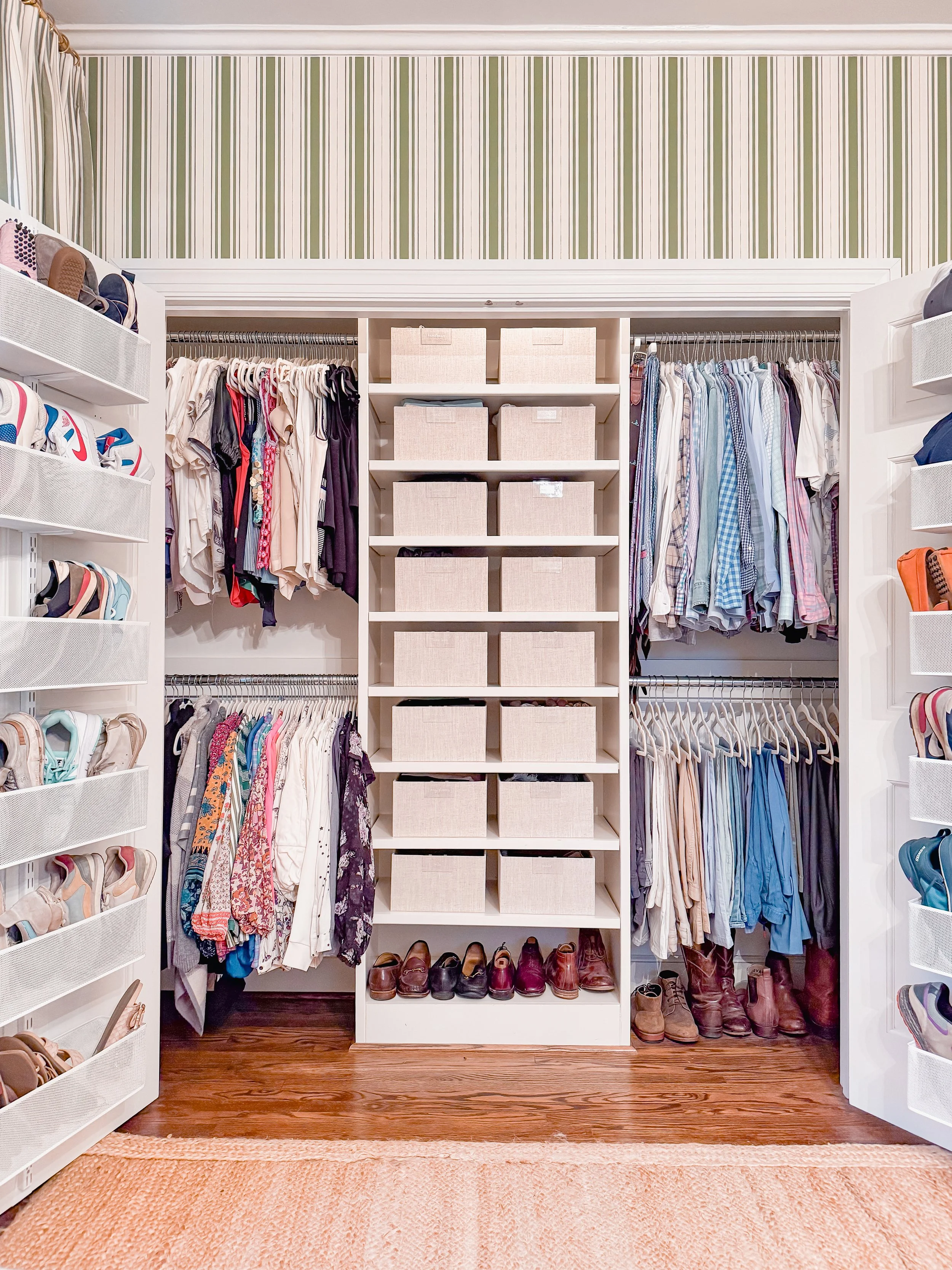 Closet with organized clothing, shoes, and storage bins, with striped wallpaper and hardwood floor.