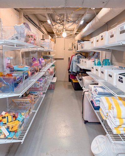 Empty storage room with wire shelves on both sides, containing various packaged goods, linens, and storage boxes.