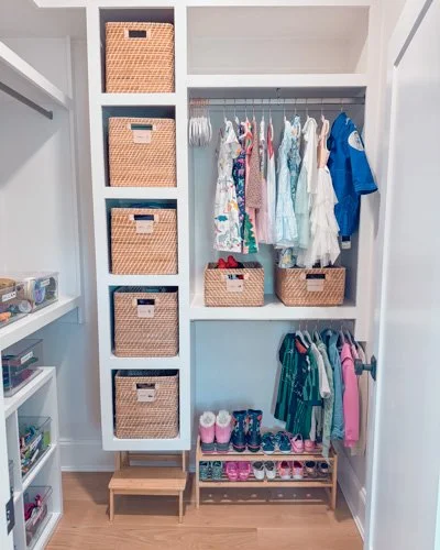 Children's closet with hanging clothes, shoes, and woven baskets for storage.
