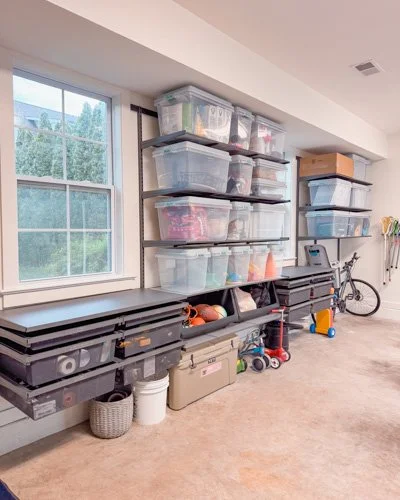 Garage with storage shelves holding plastic bins, a workbench with tools, and a bicycle.