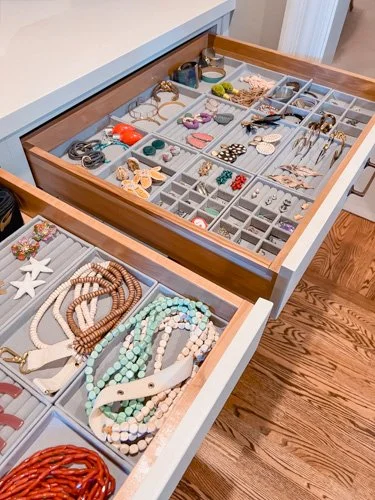 Open jewelry drawer with various necklaces, earrings, and rings organized in compartments.