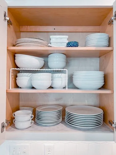 Open kitchen cabinet filled with various white and blue dishes and bowls on three shelves.