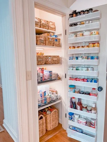 Pantry with shelves filled with food and condiments, with an organized door-mounted spice rack containing various jars and containers.