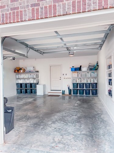 Empty garage with storage shelves, clear plastic bins, and a concrete floor.