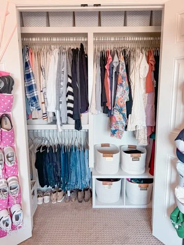 Open closet with hanging clothes, stacked shoes, and storage bins