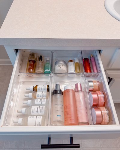 Open bathroom drawer containing various skincare and cosmetic products such as bottles, jars, and tubes.
