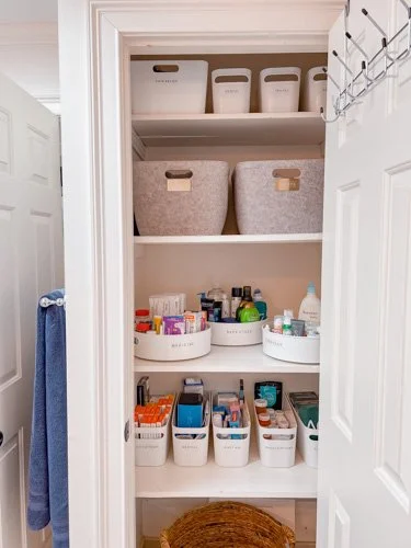 Closet with organized shelves containing storage bins, baskets, and bottles, with a blue towel hanging on a hook on the door.