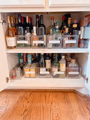 A kitchen cabinet with two shelves containing various liquor bottles and organized containers with labels.