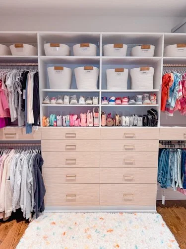 Walk-in closet with organized shelves and drawers, containing storage baskets, shoes, and clothing on hangers.