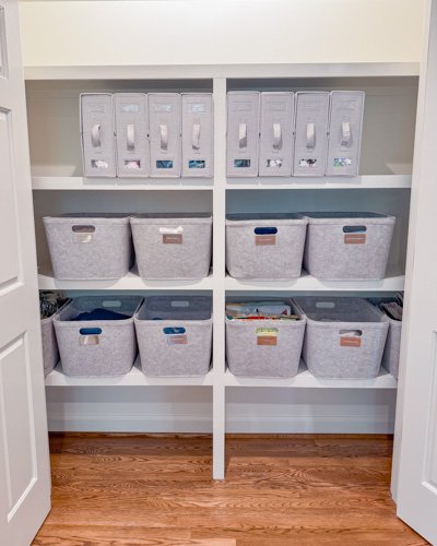 White shelving unit with six gray storage bins on wooden floor.
