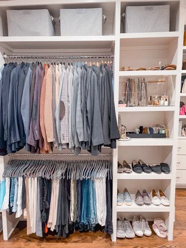 Closet with hanging shirts and pants, organized shelves with bags, shoes, and accessories, and storage bins at the top.