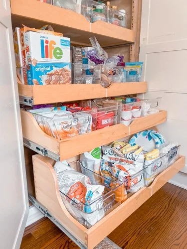A pull-out pantry drawer with various snacks like chips, crackers, and sweets in plastic bags and boxes.