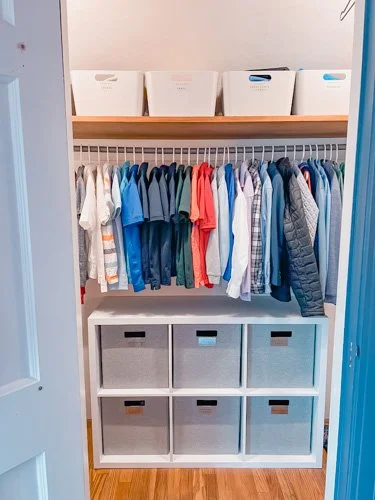 Closet with hanging children's clothes, storage boxes on shelf, and plastic bins at the bottom.