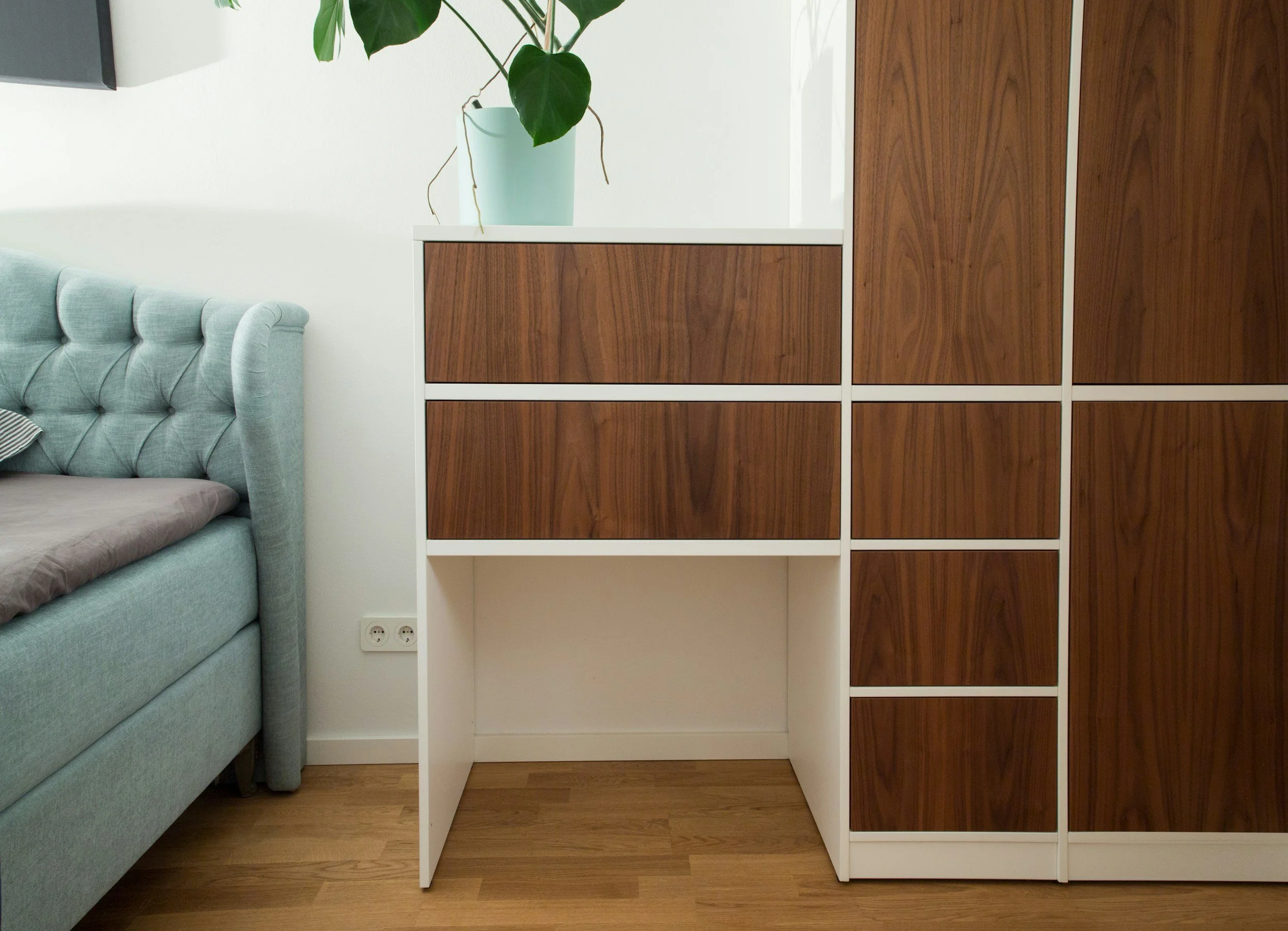 A modern interior with a light blue tufted sofa, wooden cabinet with white frame, a potted plant, and hardwood flooring.