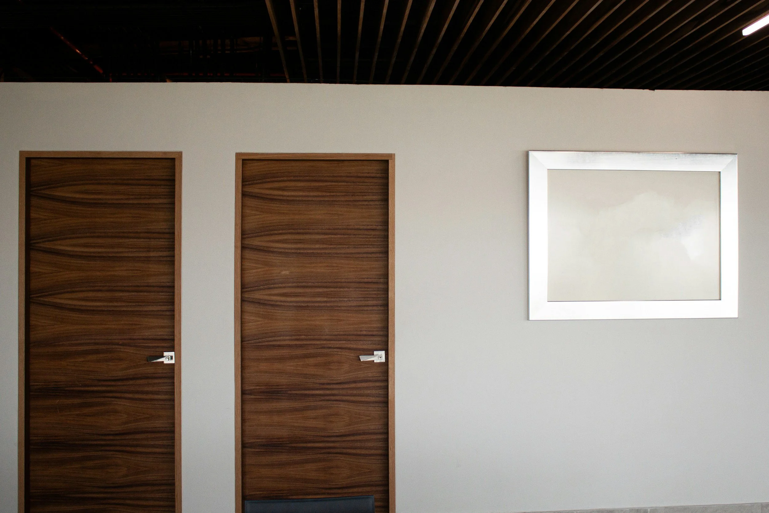 Two wooden doors and a mirror on a light-colored wall, with a black chair partially visible at the bottom.