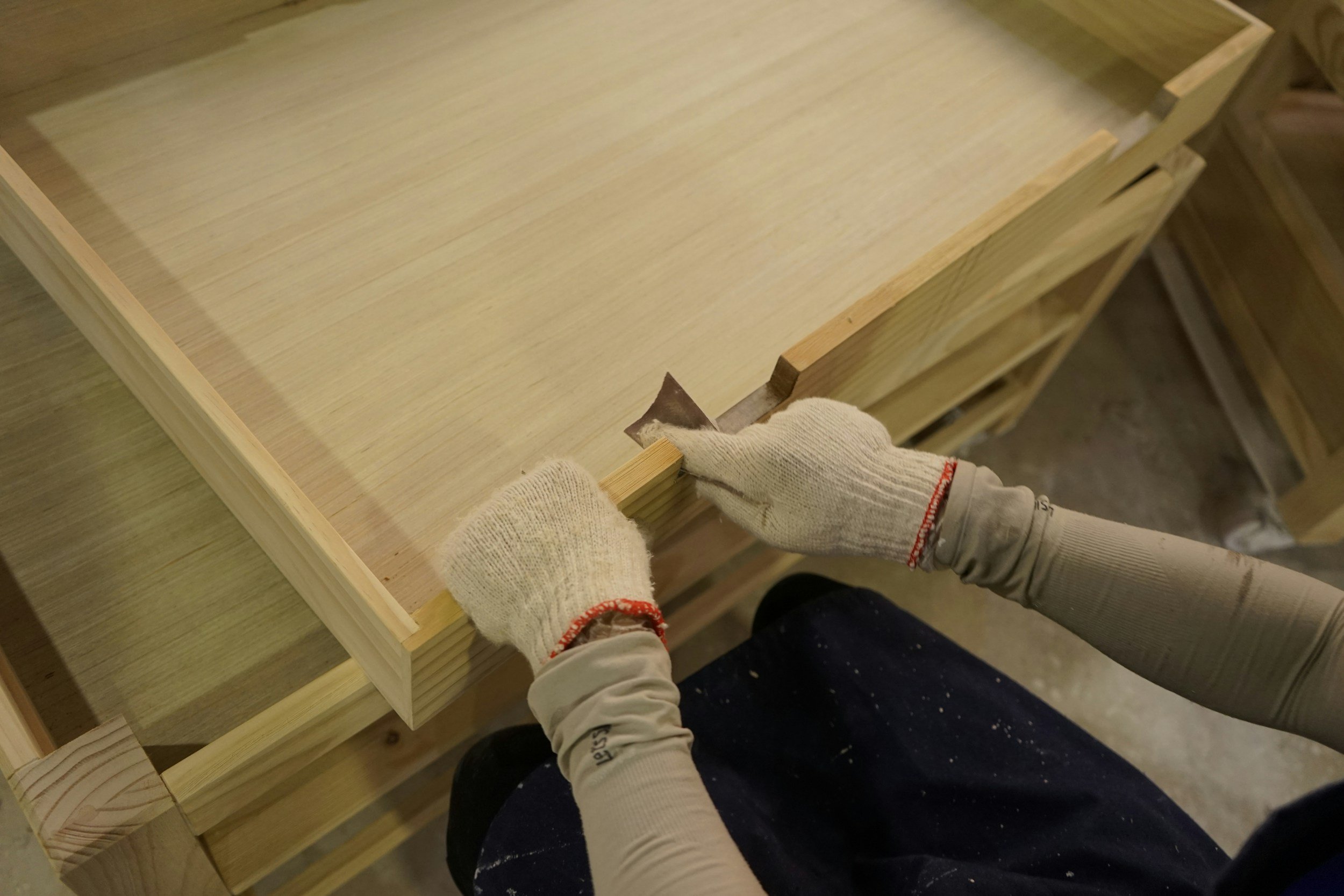 Person woodworking, sanding a wooden surface with a hand sander in a woodworking shop.