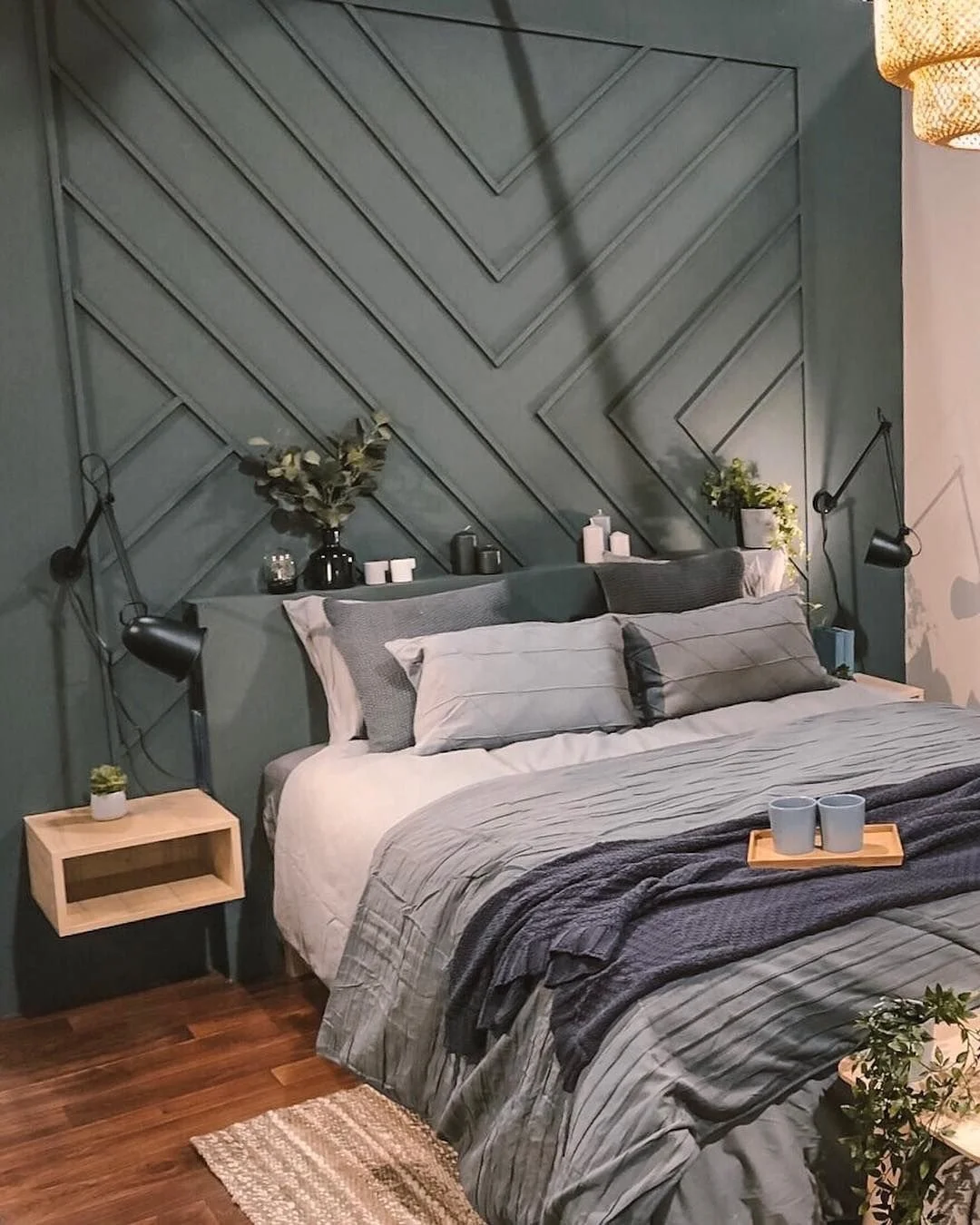 A modern bedroom with a gray accent wall featuring diagonal paneling, a bed with gray and white bedding, wall-mounted lamps, and small decor and plants on nightstands.