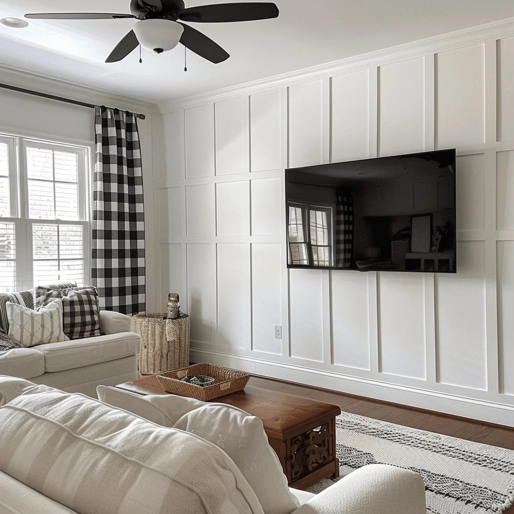 Living room with white paneled walls, a wall-mounted television, a ceiling fan, large windows with black and white checkered curtains, and white sofas with checkered pillows.