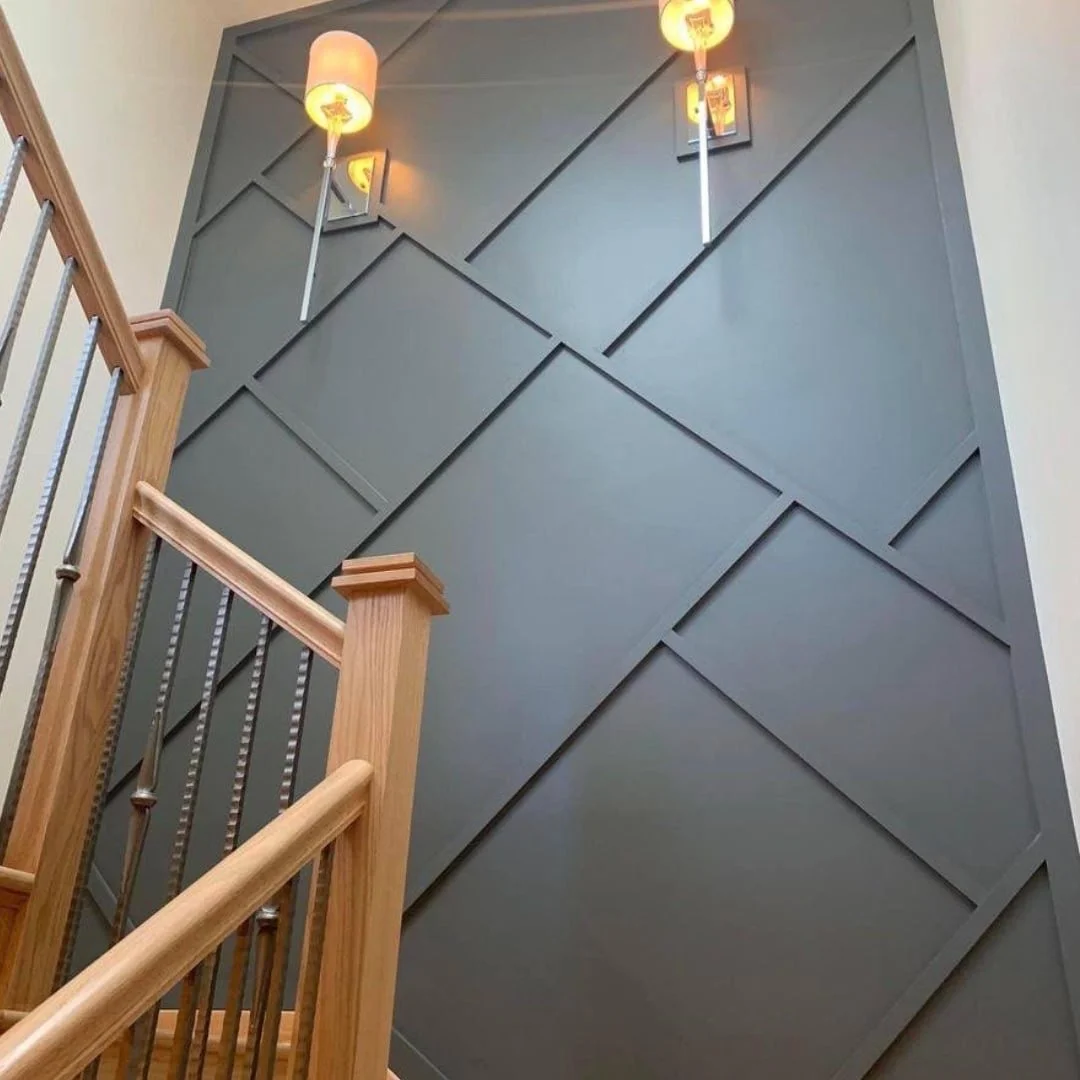 Interior staircase with wooden handrail and metal balusters, gray wall with a geometric pattern, and two wall-mounted lamps with orange shades.