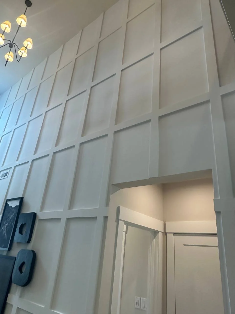 Interior wall with decorative paneling, a corner with doorway, and a ceiling chandelier with multiple light bulbs.
