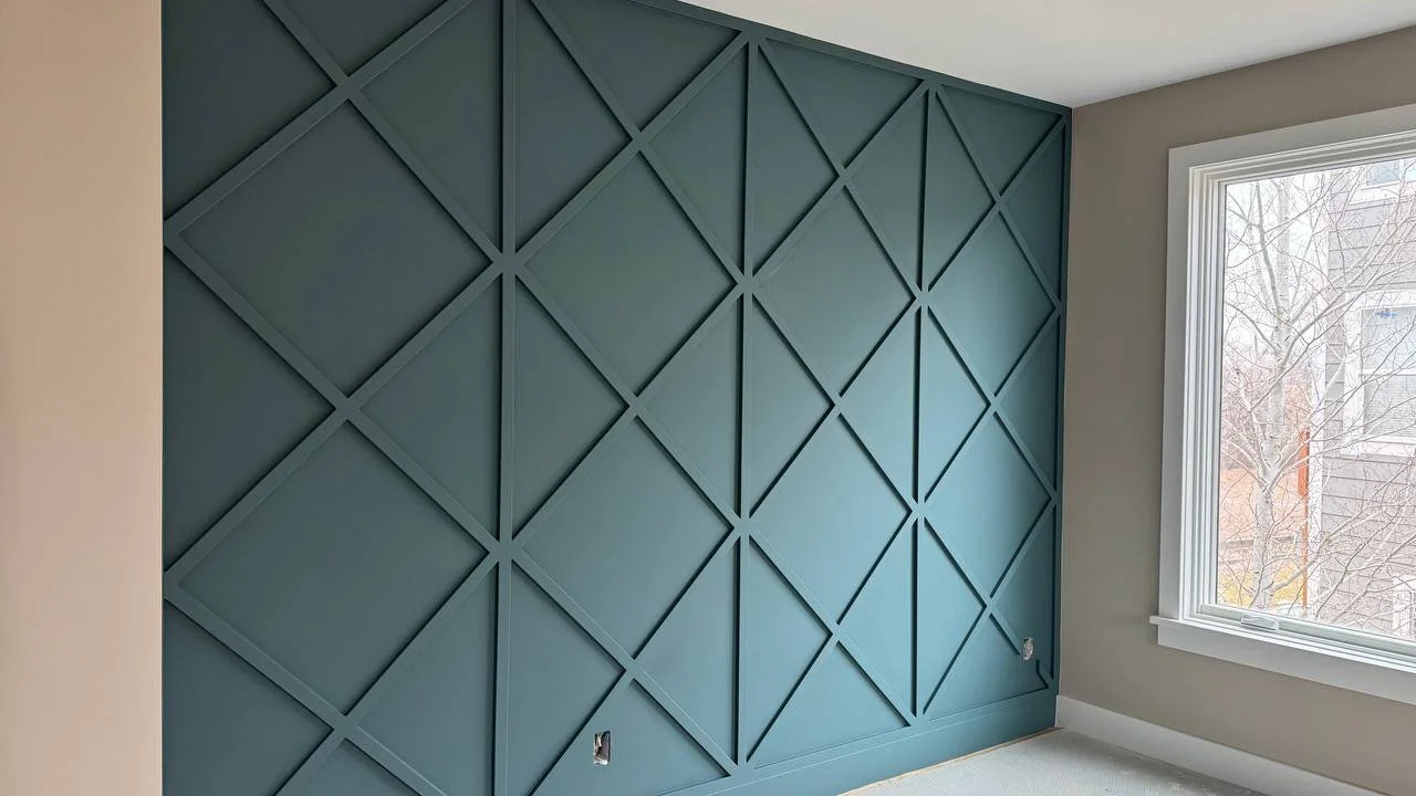 Interior of a room with a blue accent wall featuring a geometric diamond pattern, a large window, and light-colored carpet.