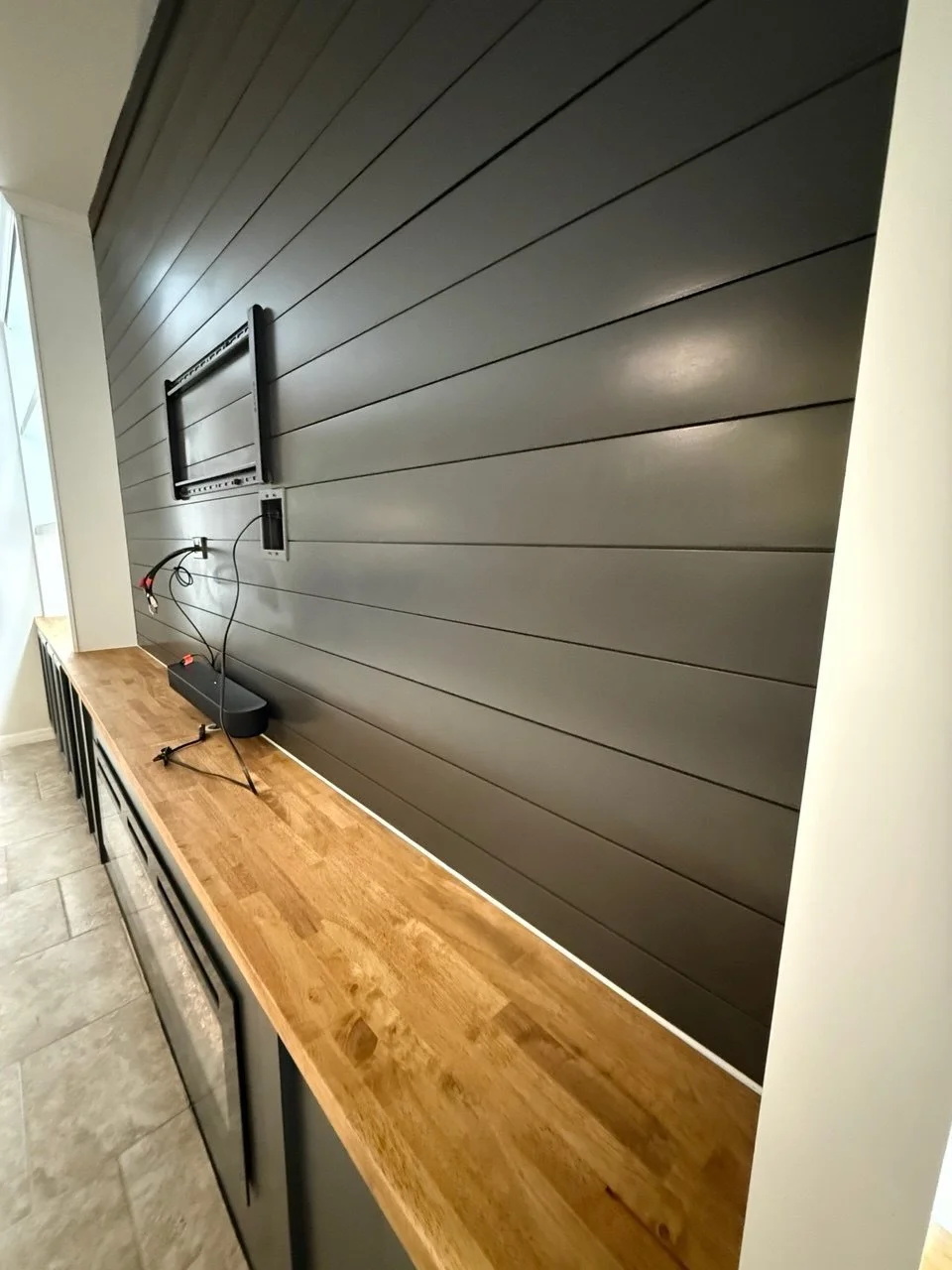 Black shiplap accent wall prepared for TV installation above custom cabinets