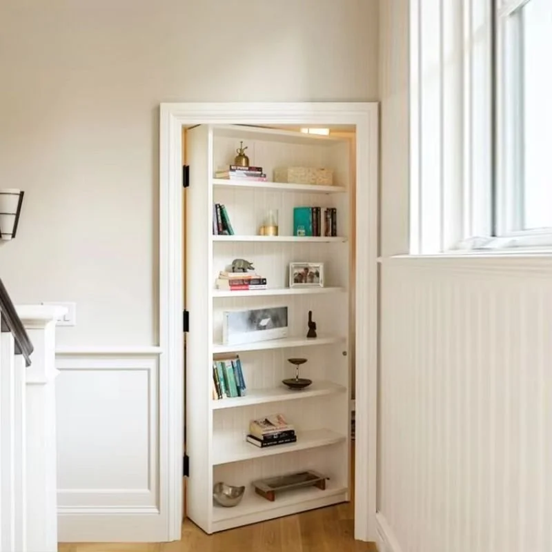 White bookshelf with decorative items and books in a bright room near a window.