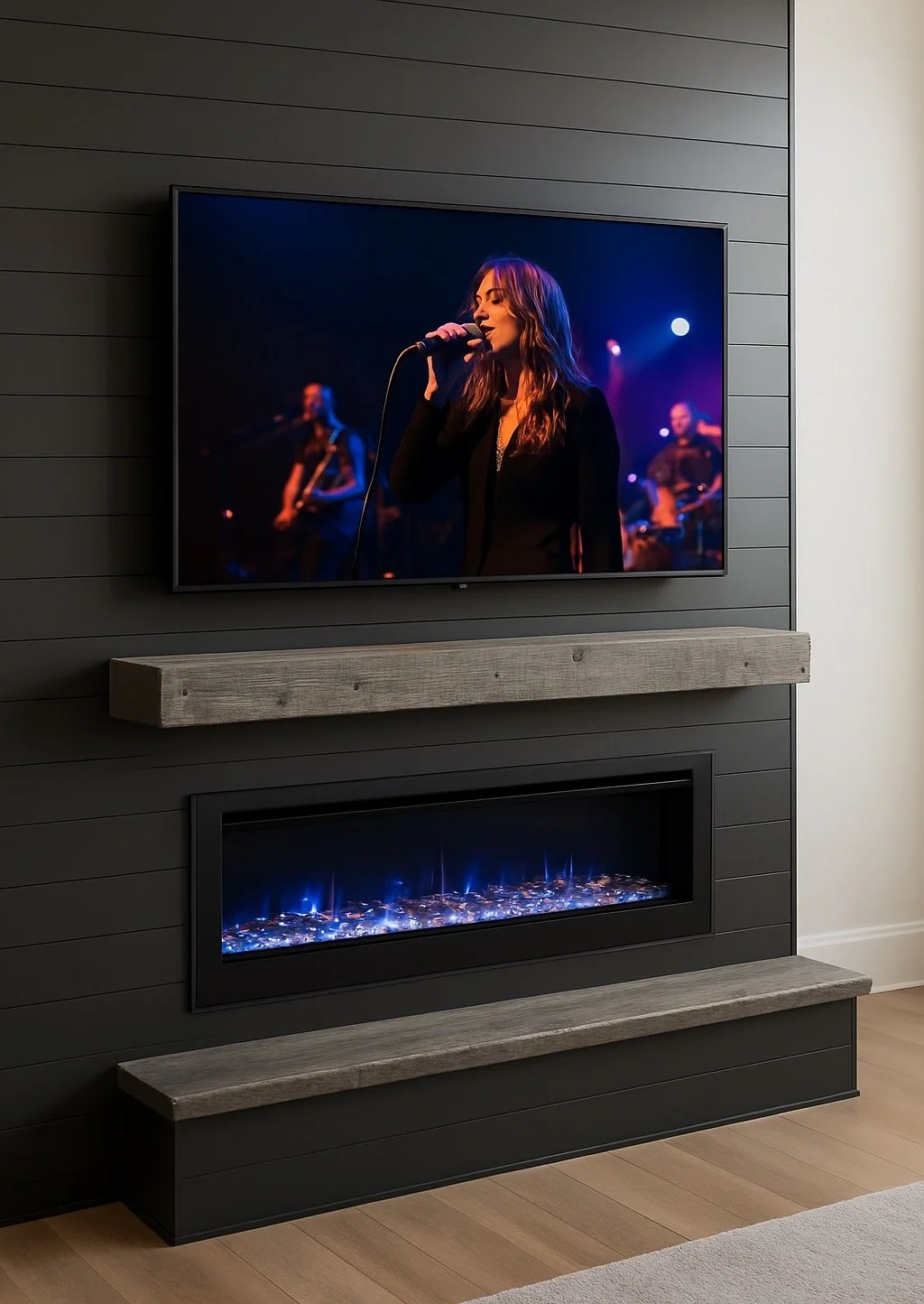 A wall-mounted flat-screen TV displaying a female singer performing with a band in a dark, colorful concert setting, above a modern fireplace with blue flames, all set against a dark gray paneled wall with a wooden mantel.