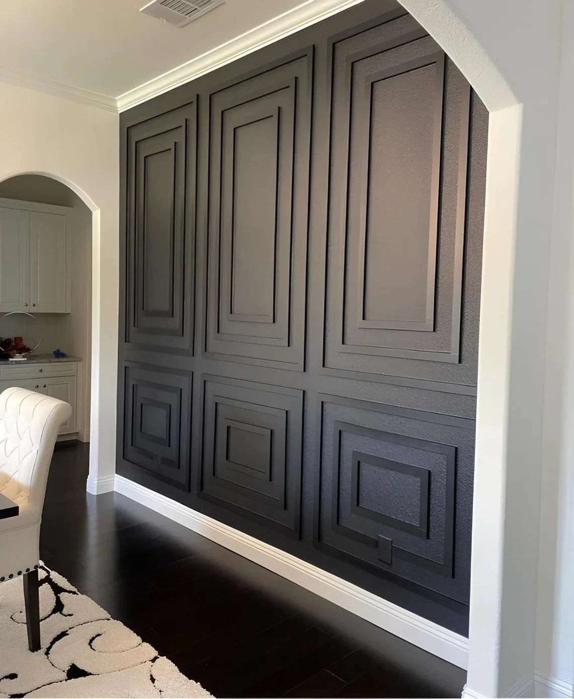 Close-up view of a large, black, paneled wooden wall or cabinet with decorative molding, in a room with dark hardwood floor and white trim.