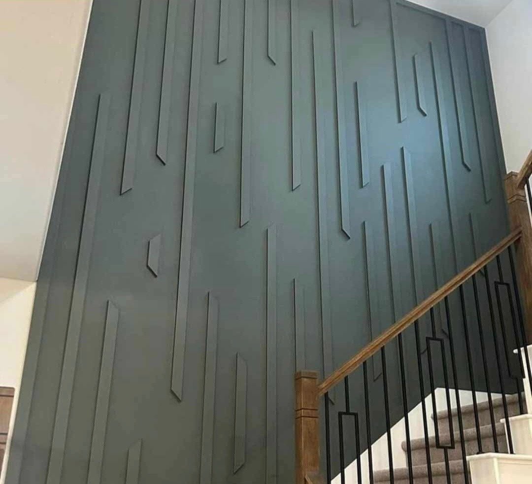 Interior wall featuring modern geometric wall panel design with vertical and angular elements, adjacent to staircase with wooden handrail and black metal balusters.