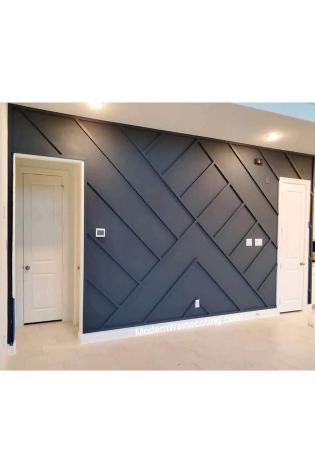 Interior wall with geometric black wooden paneling in a modern room, with two white doors on either side, light-colored flooring, and recessed ceiling lights.
