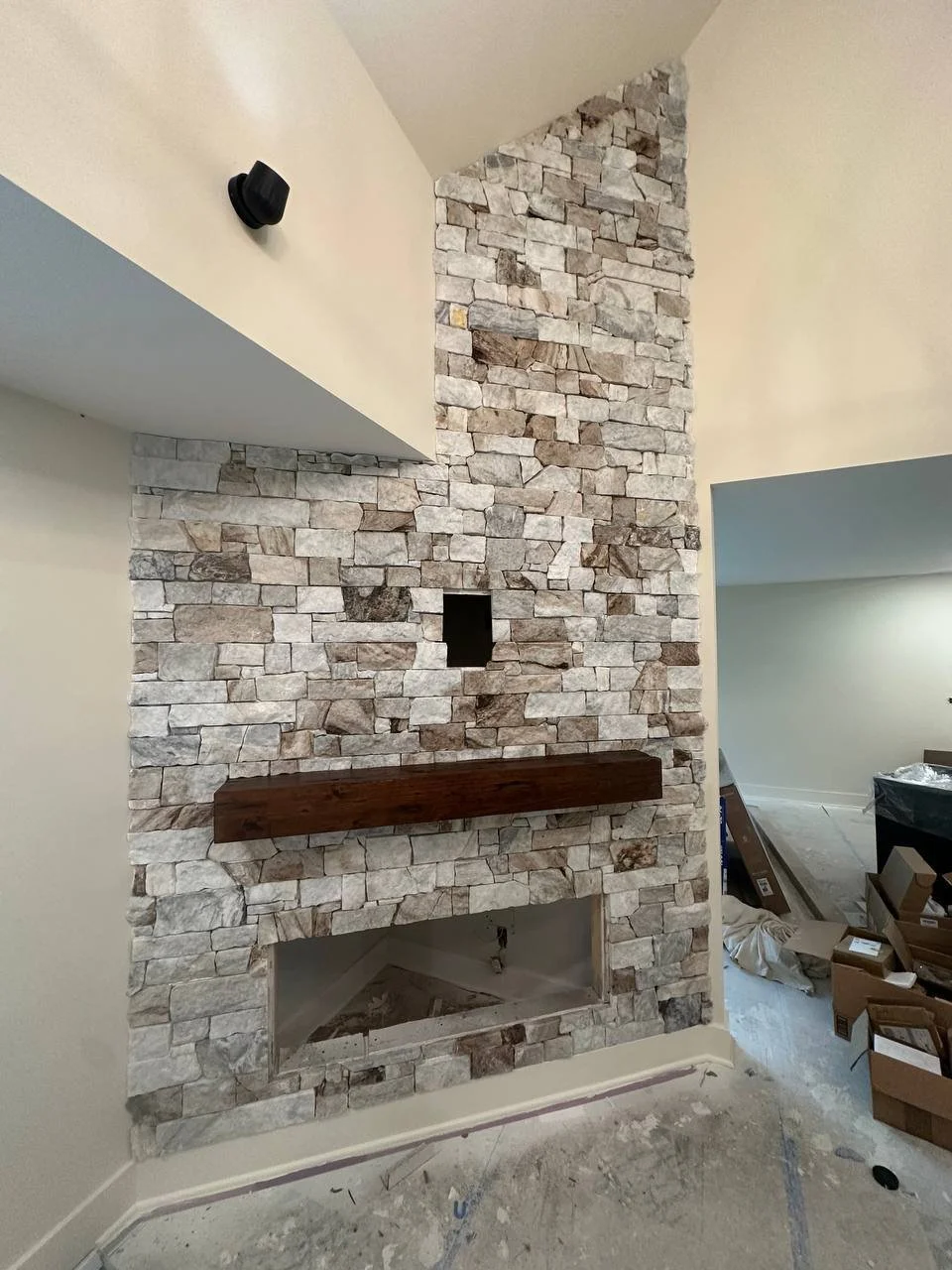 Interior view of a stone fireplace with a wooden mantel under construction, with boxes and construction materials on the floor.