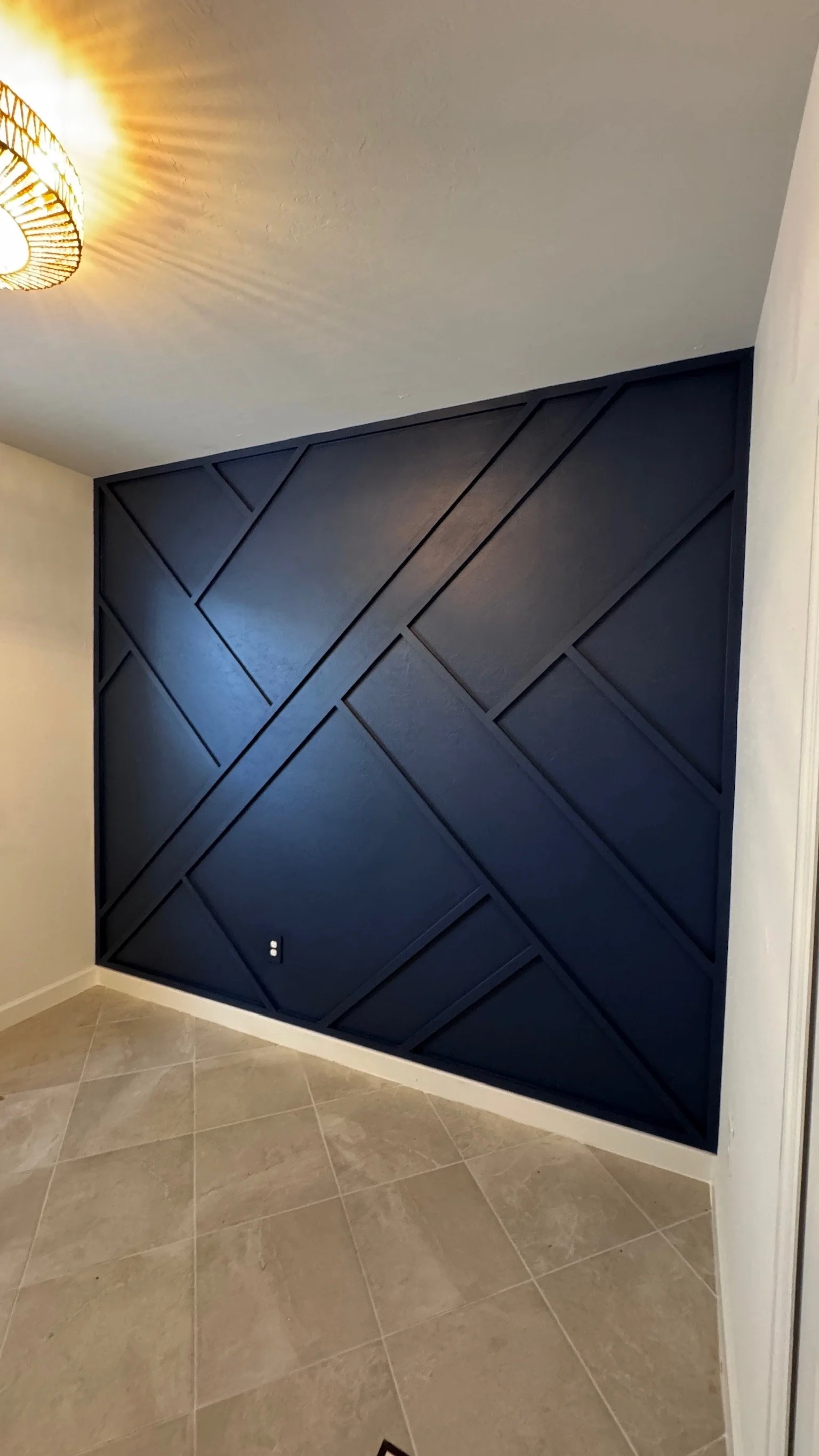 A black geometric accent wall in a room with beige tiled flooring and a ceiling light.