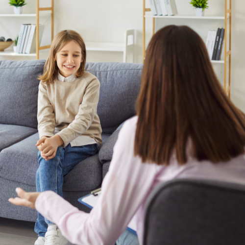 A girl sitting on a couch, smiling and talking to a woman sitting in front of her in an office setting.