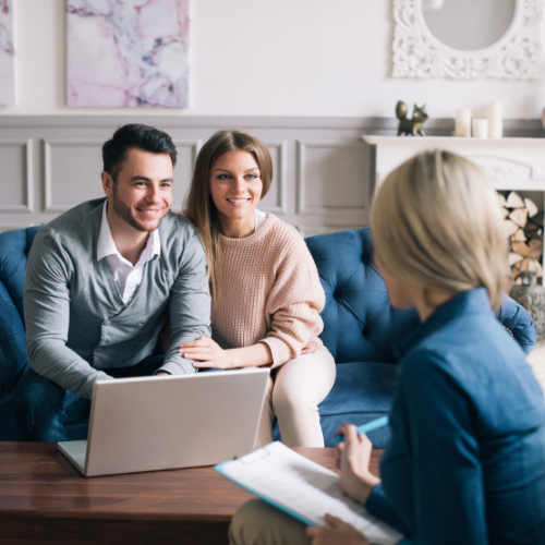 A couple sitting on a blue couch during a home consultation with a professional woman taking notes.