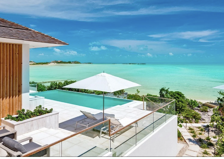 Ocean view from a luxury vacation home with a private pool, sun loungers, an umbrella, and greenery.