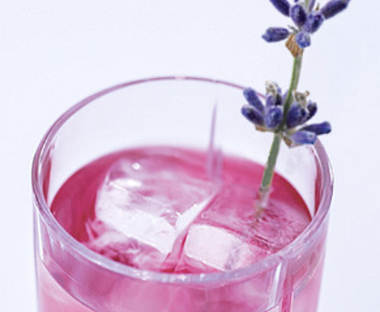 Pink-colored beverage with ice cubes in a clear glass, garnished with a sprig of purple lavender.