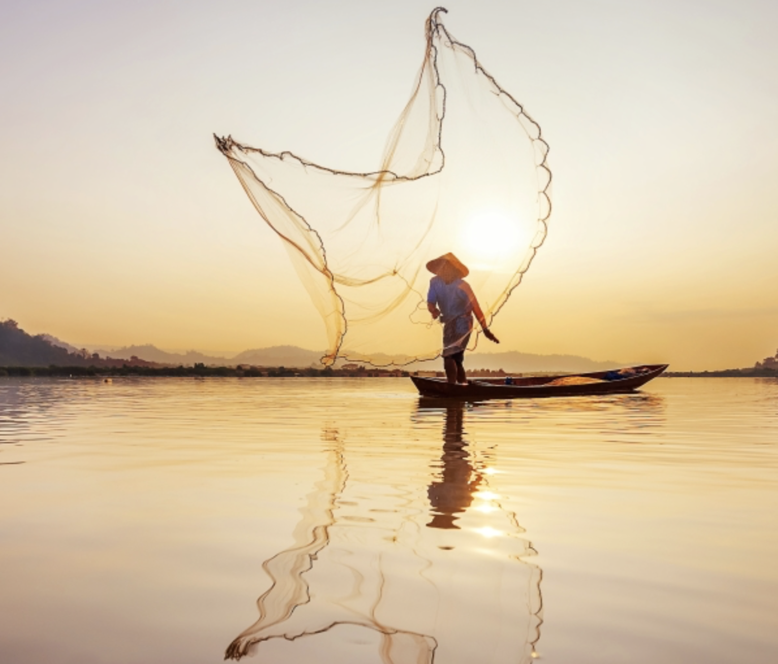 A person standing on a boat fishing with a net during sunset on a calm body of water.