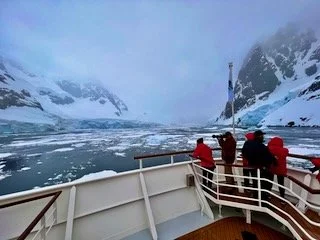 Group of people on a boat viewing icy mountains and glaciers in a cold, foggy landscape.