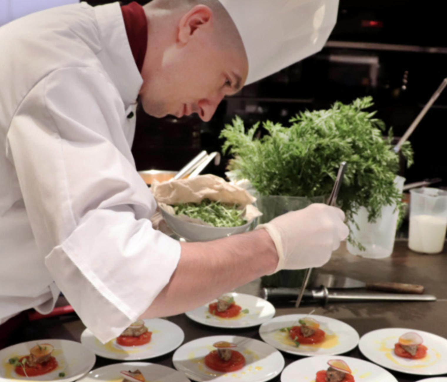 Chef garnishing multiple plates of Gourmet appetizer with herbs and sauce at a restaurant kitchen.