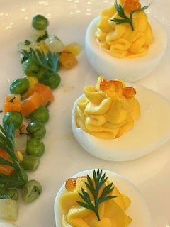 Deviled eggs garnished with herbs and orange zest, with a side of chopped carrots and green peas.