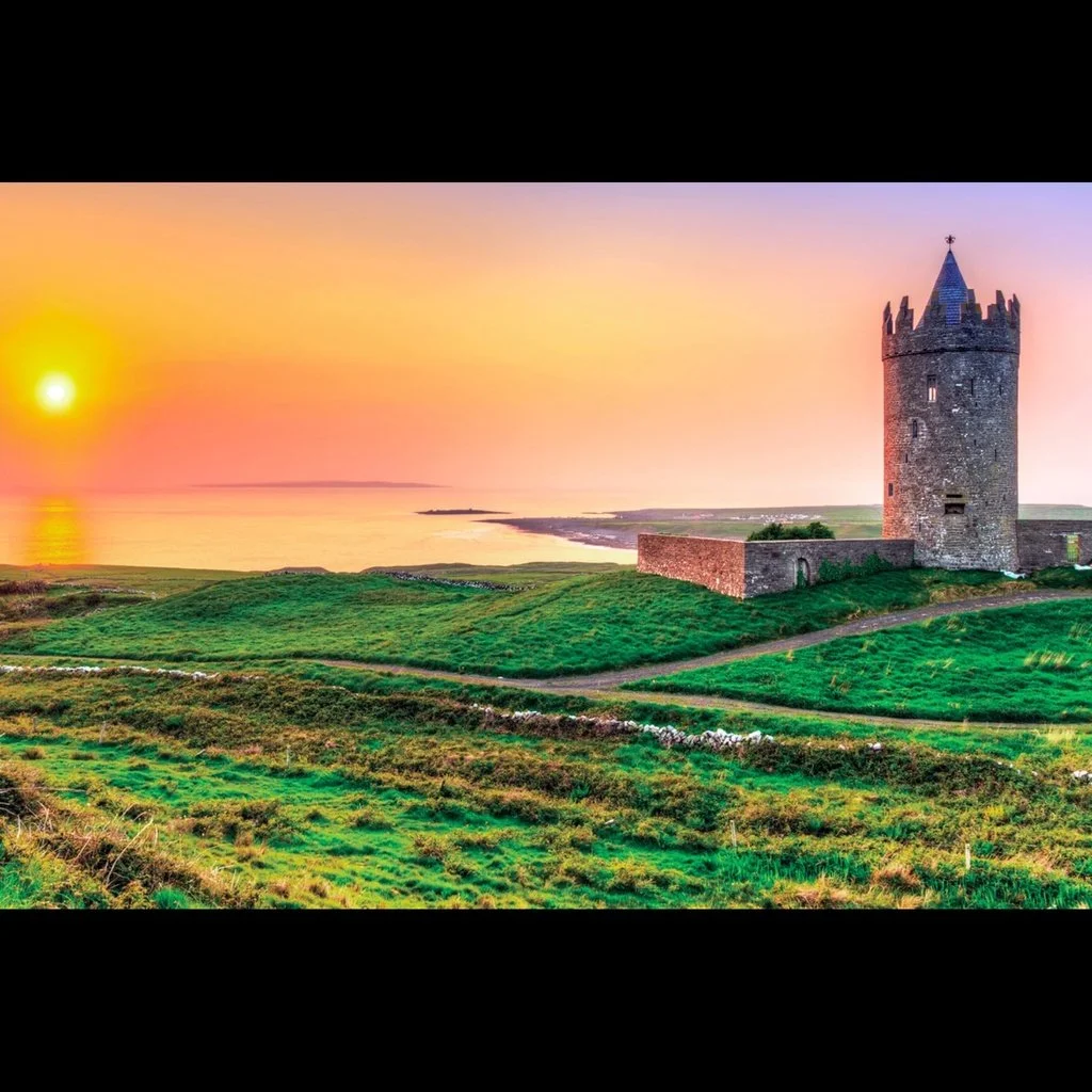 Scenic view of a coastal landscape with a historic stone tower on a grassy hill at sunset or sunrise.