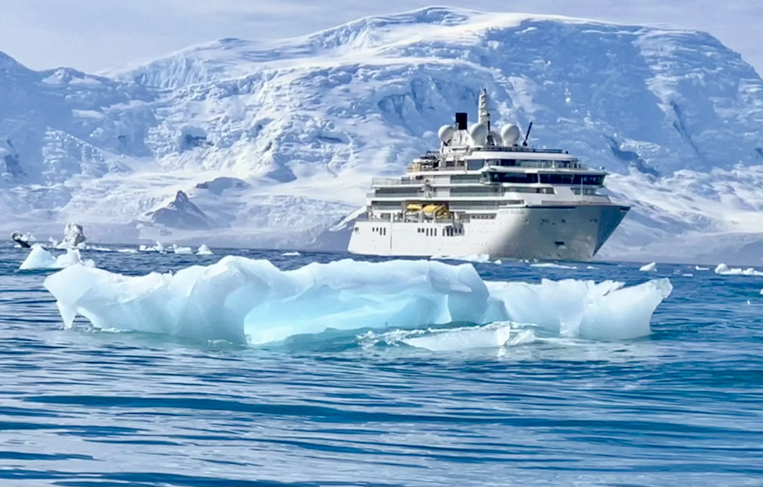 A cruise ship sailing in icy waters with icebergs and snow-covered mountains in the background.