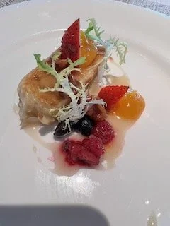 Dessert plate with a pastry topped with strawberries, orange slices, and garnished with whipped cream, berries, and edible leaves.